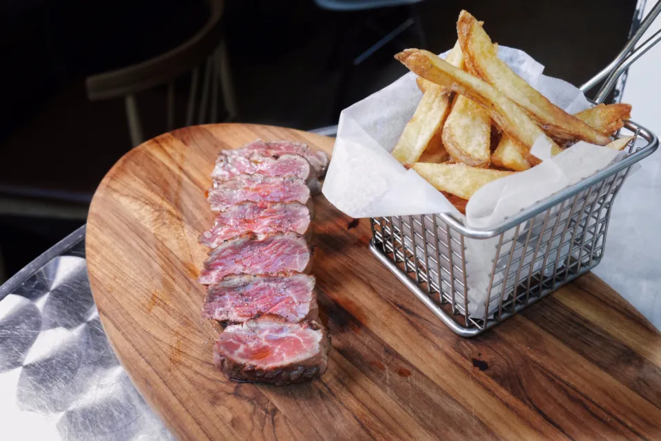 Sliced medium-rare beef steak on a wooden board with fries